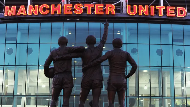 imagem da fachada do manchester united com tres pessoas a frente
