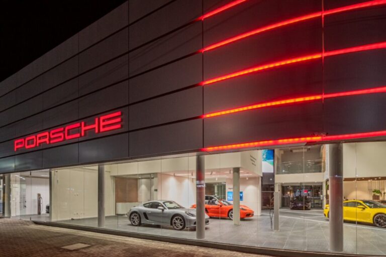 A imagem mostra uma concessionária da Porsche a noite com fachada iluminada m vermelho